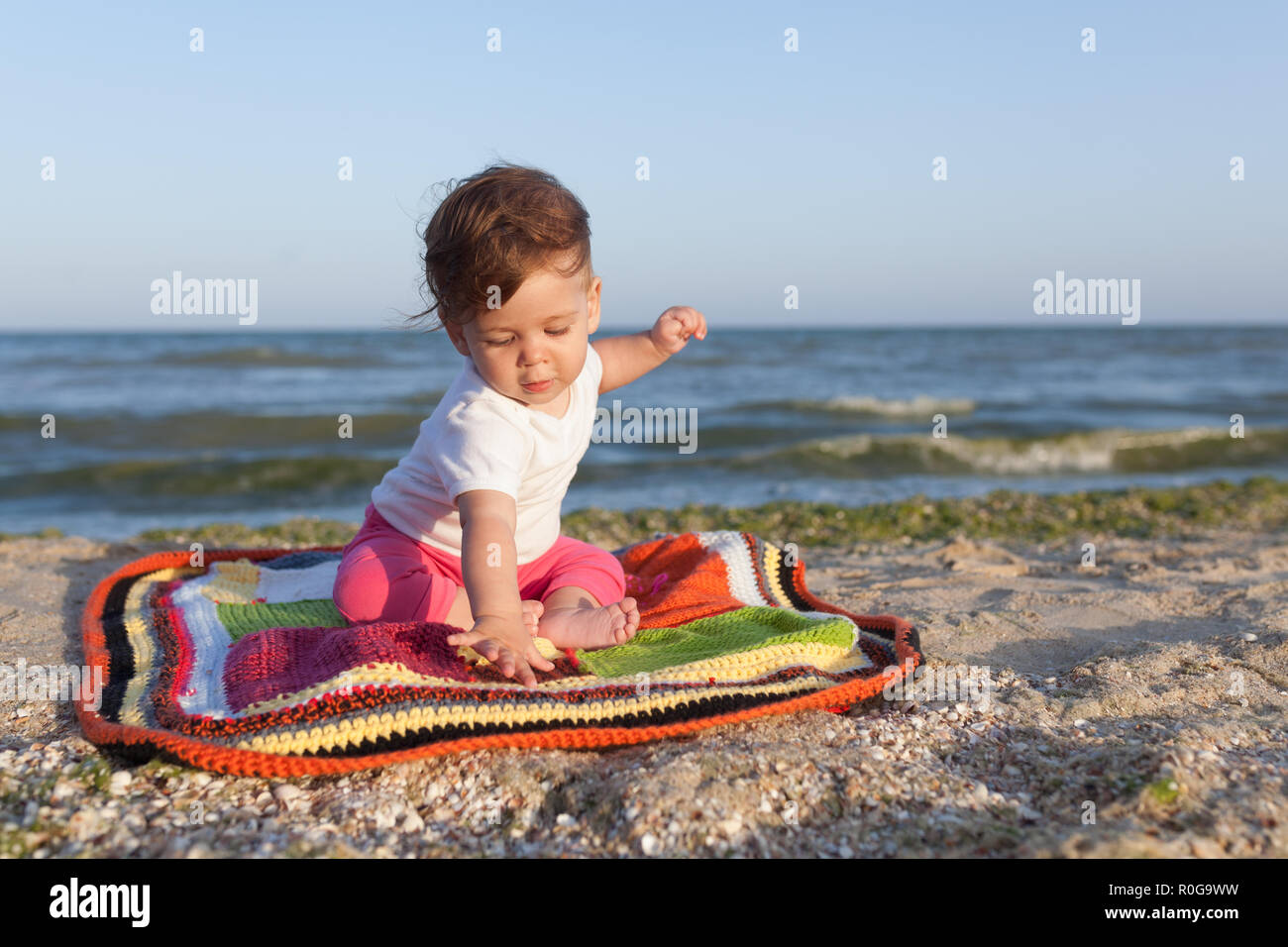 little child sitting on a colored rug on the seashore cheerful and