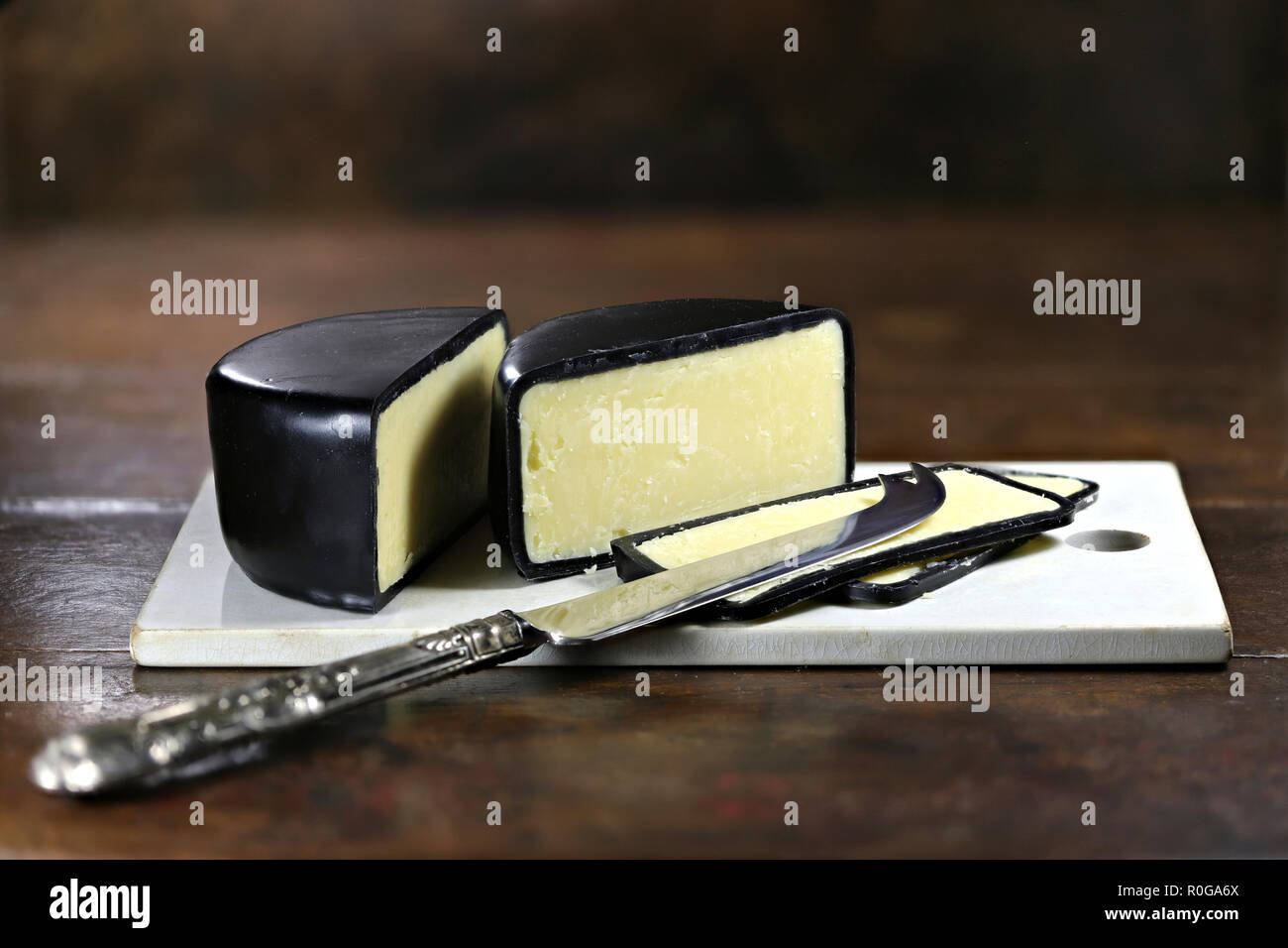 mature cheddar cheese with silver knife and ceramic cutting board isolated on rustic wooden background Stock Photo