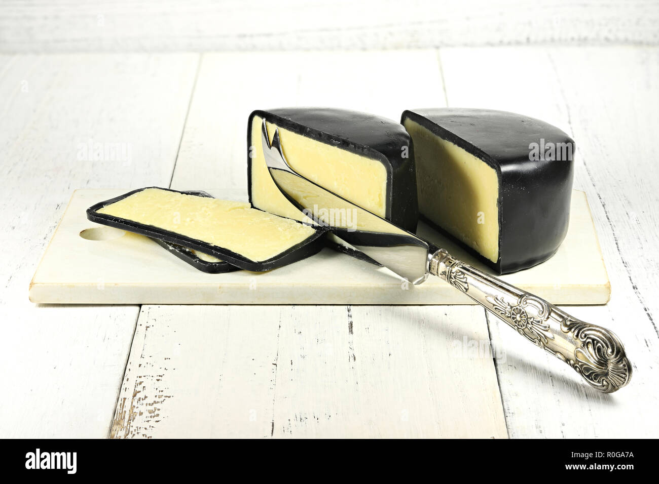 mature cheddar cheese with silver knife and ceramic cutting board isolated on wooden background Stock Photo