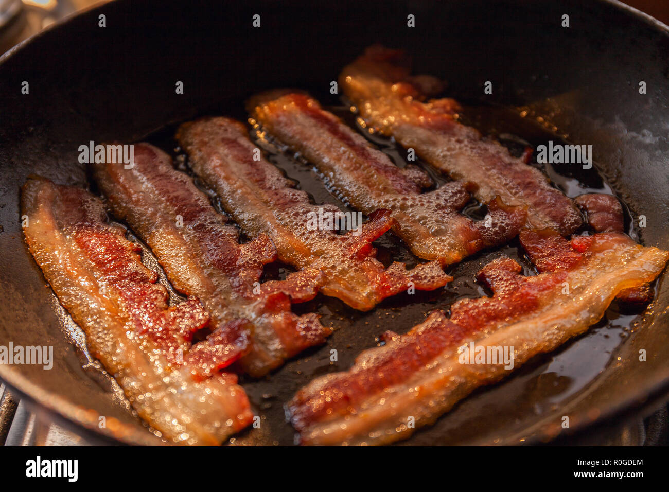 Bacon strips or rashers cooked in frying pan in the rays of sunlight Stock Photo