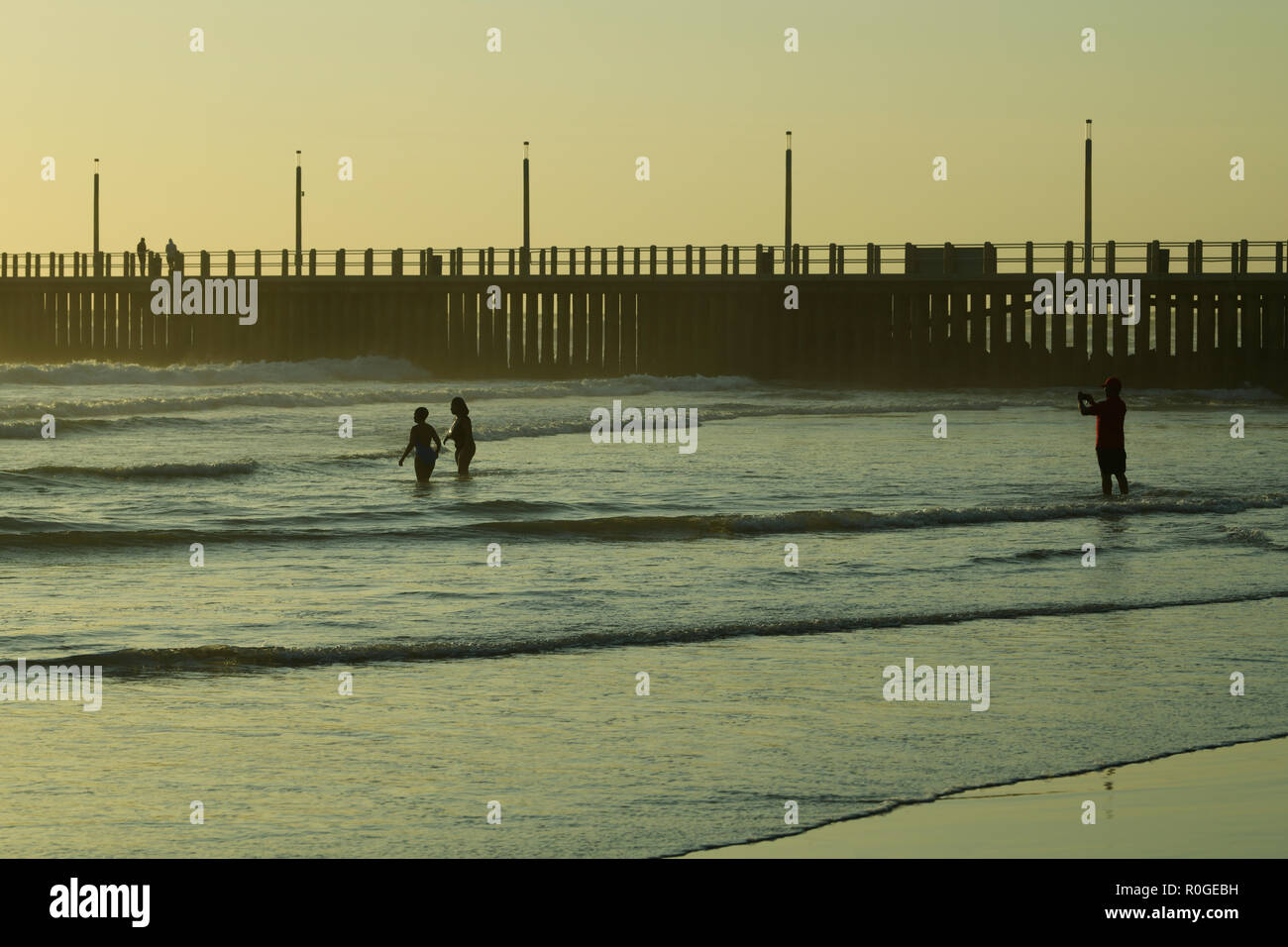 Durban, KwaZulu-Natal, South Africa, single adult male taking photo of two women standing in water while on seaside holiday at beachfront Stock Photo