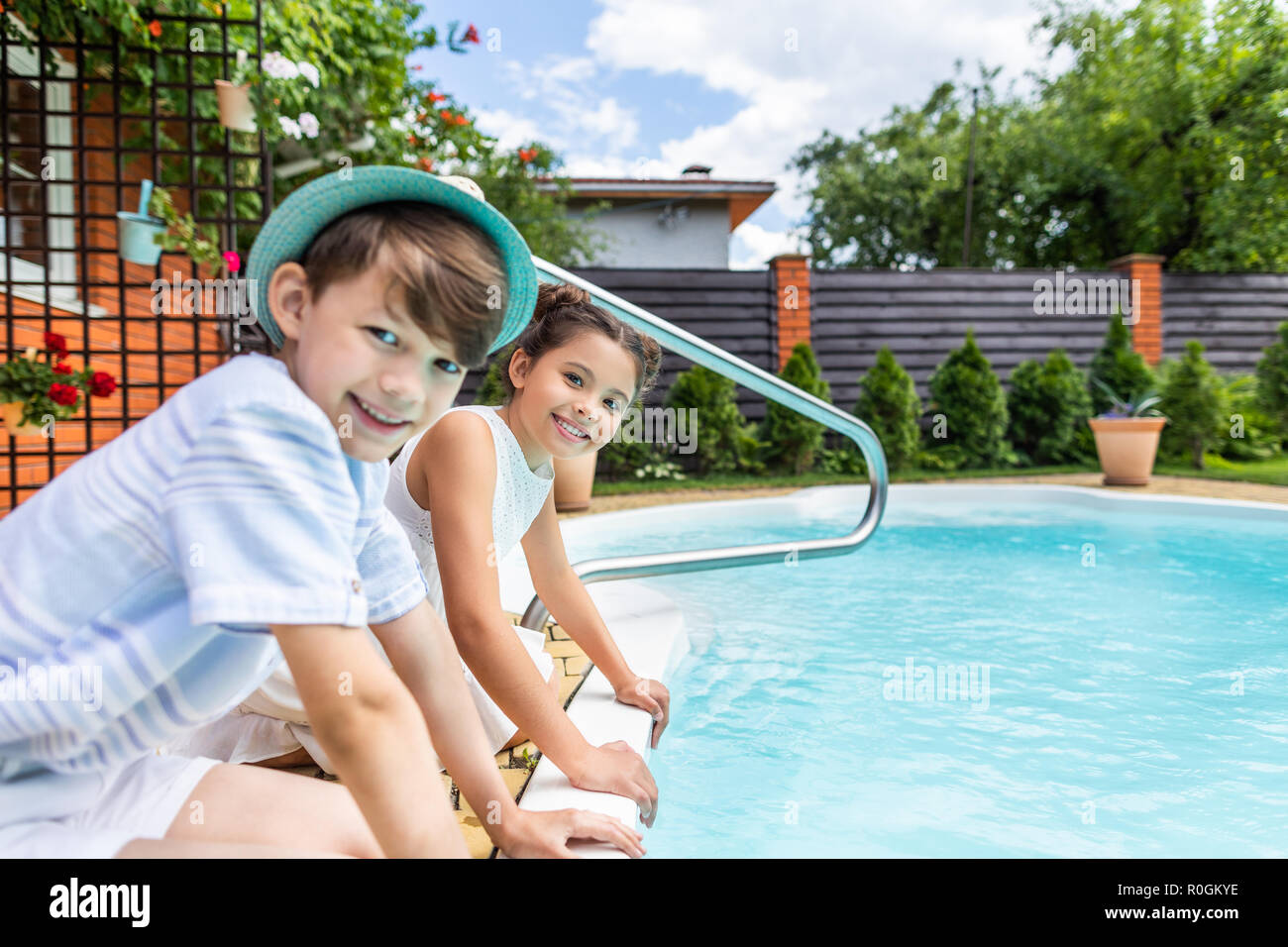 side view of little siblings sitting near swimming pool on summer day