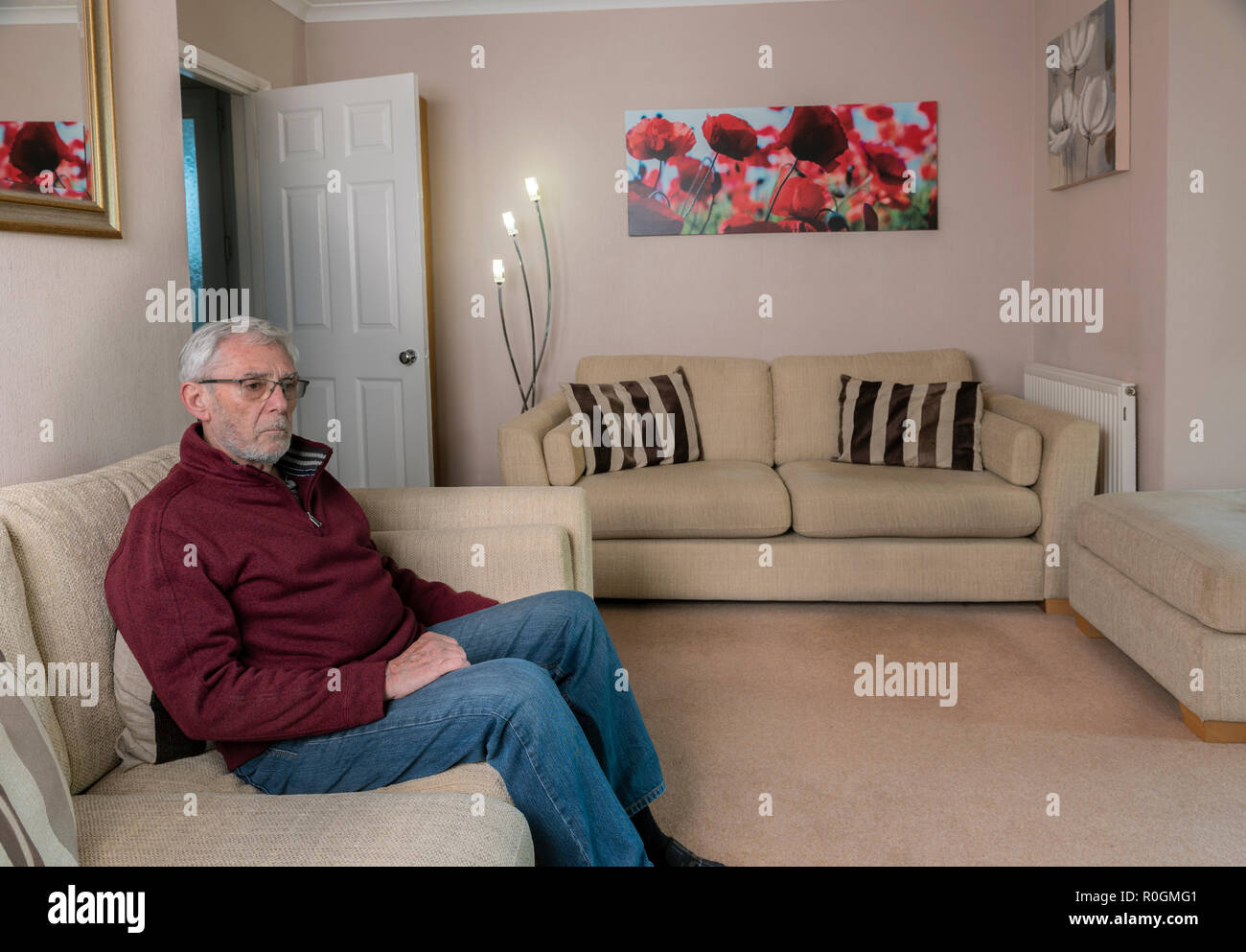 Senior man sitting alone on sofa, grieving after losing a loved one. Loneliness sad and sadness. Stock Photo