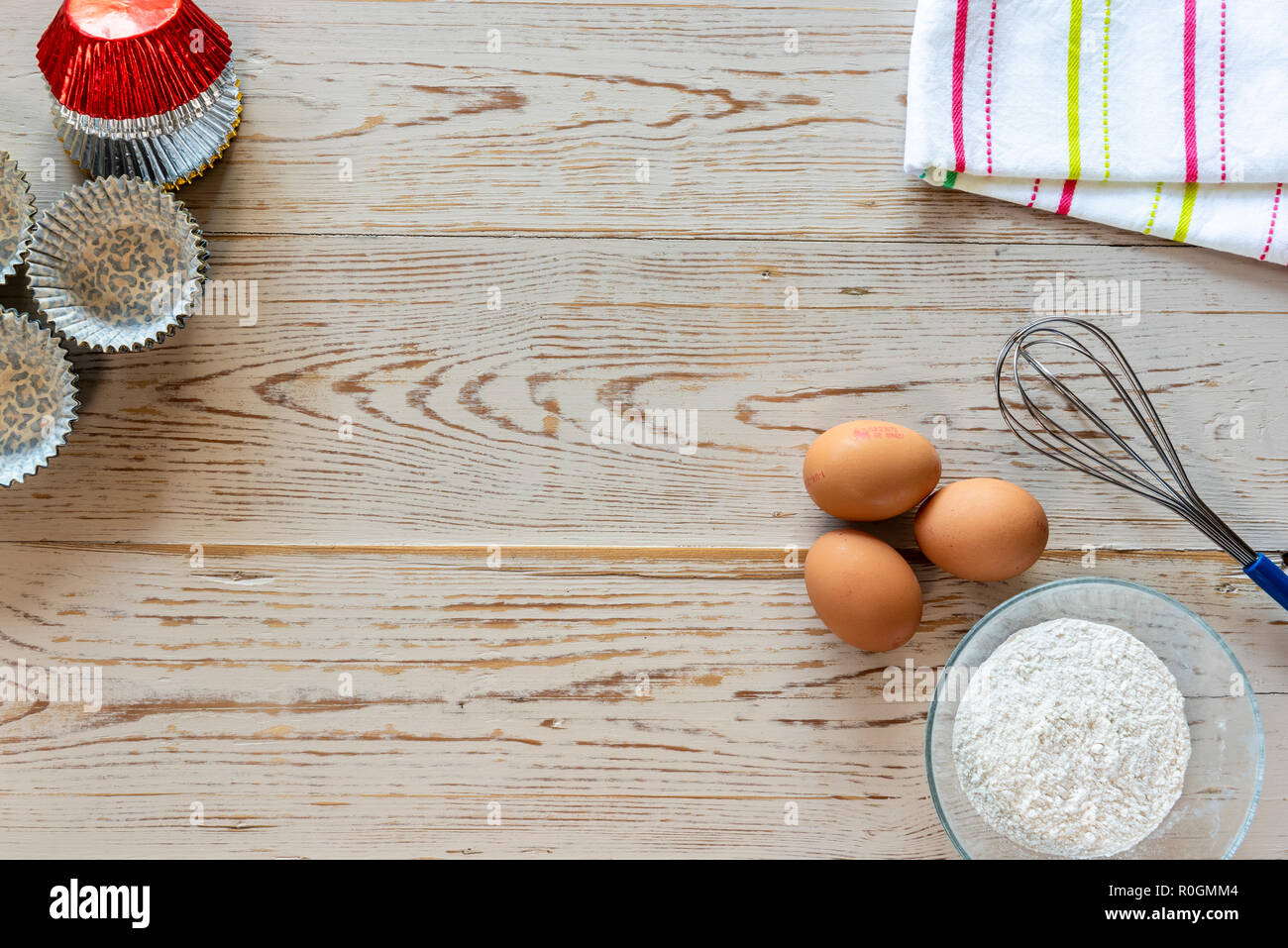 Baking ingredients, flour eggs with whisk from overhead. Cupcake cases. Stock Photo