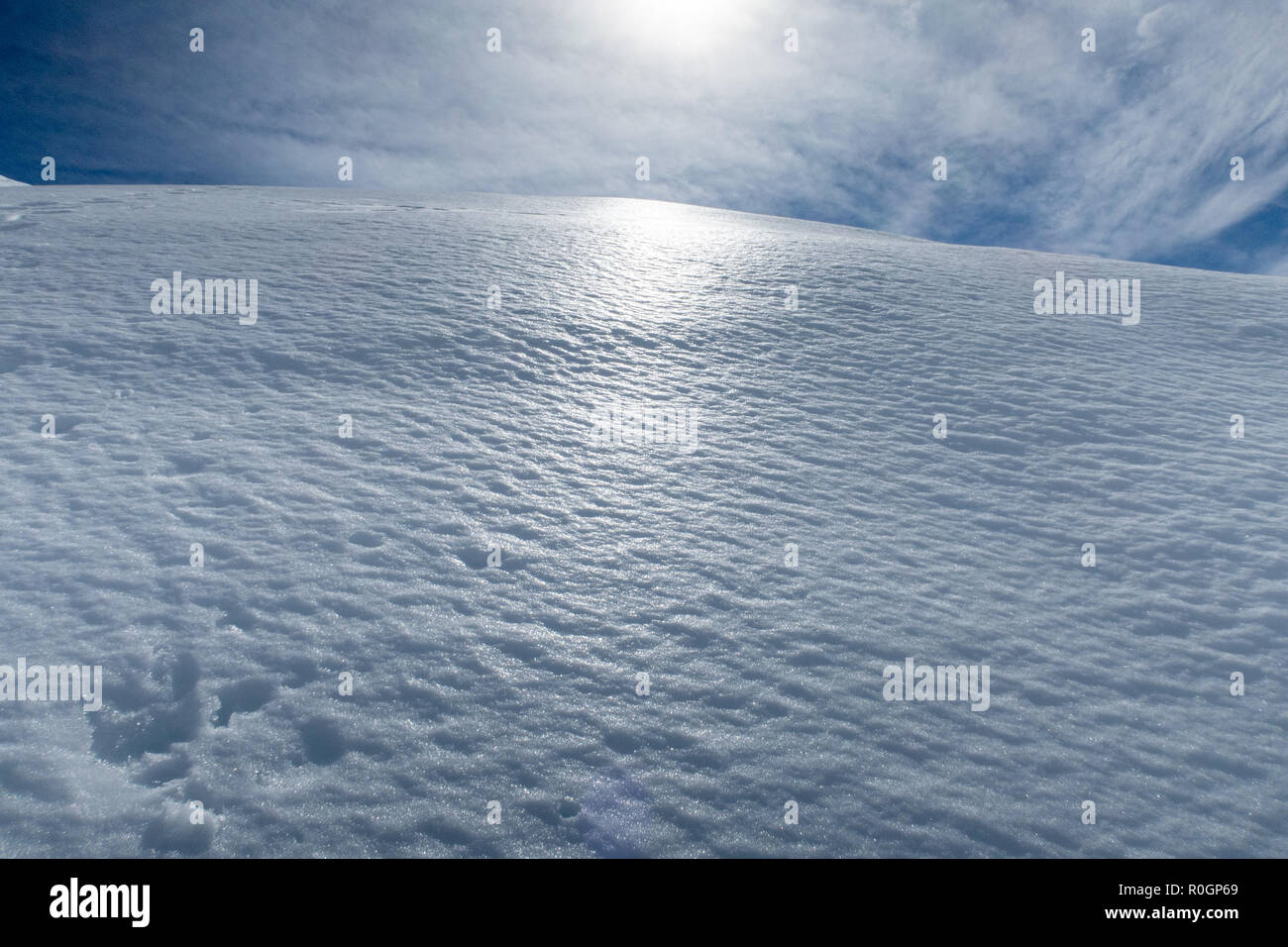 The sun shines down on spring snow on the side of a mountain in New Zealand Stock Photo