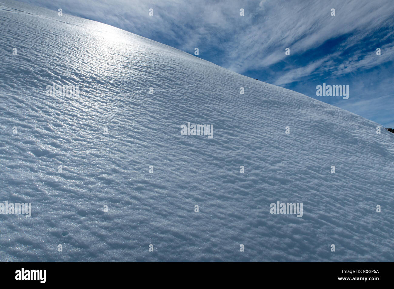 The spring snow glistens and shines in the afternoon sun on the side of a mountain Stock Photo