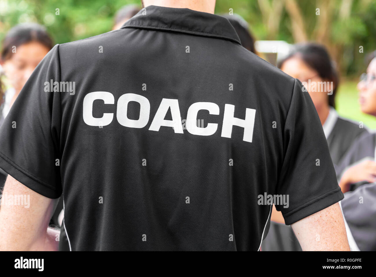 Back of sport coach wearing black COACH shirt, talking to his sport team Stock Photo