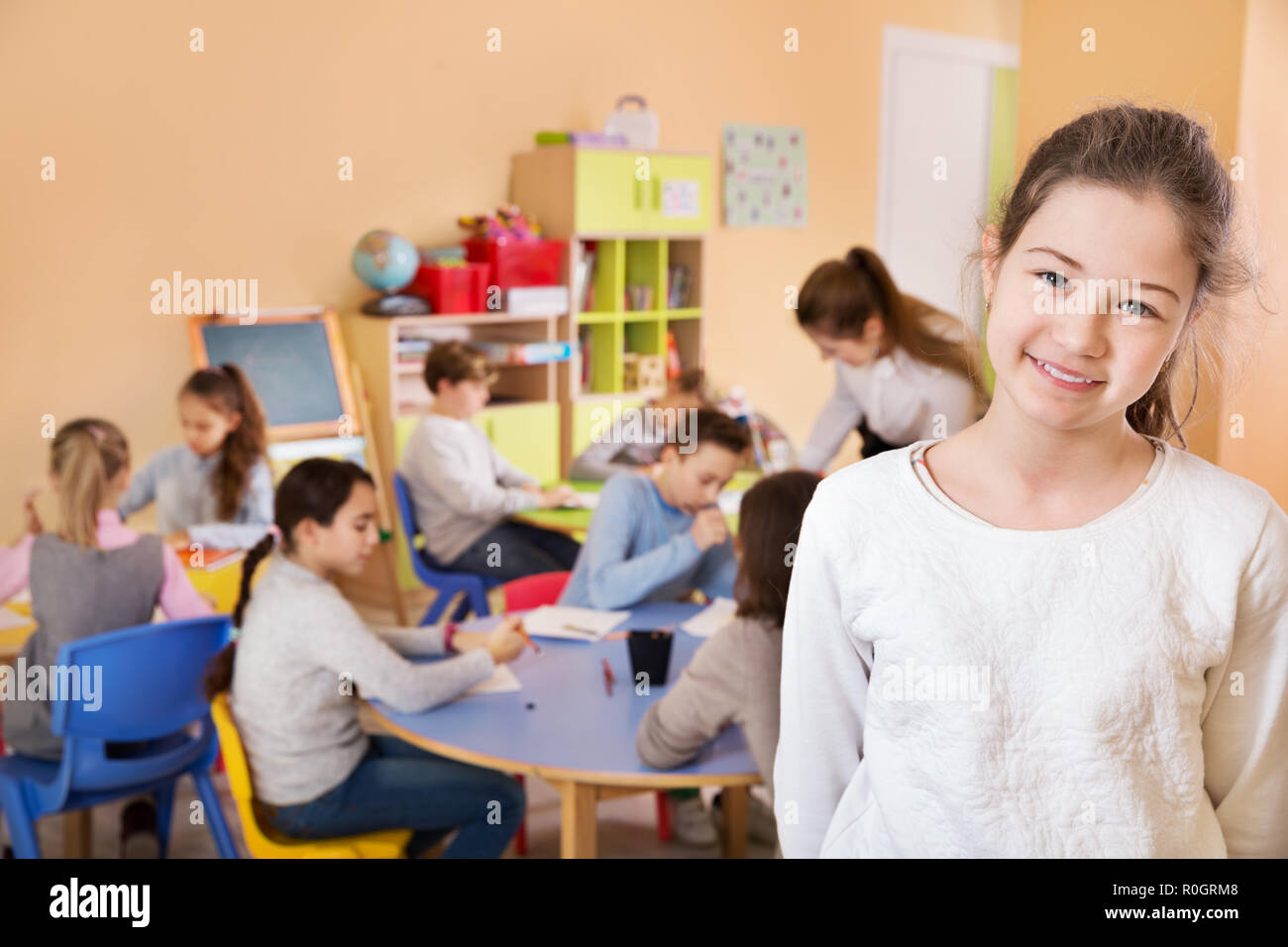 Portrait of happy schoolgirl standing foreground in classroom with ...