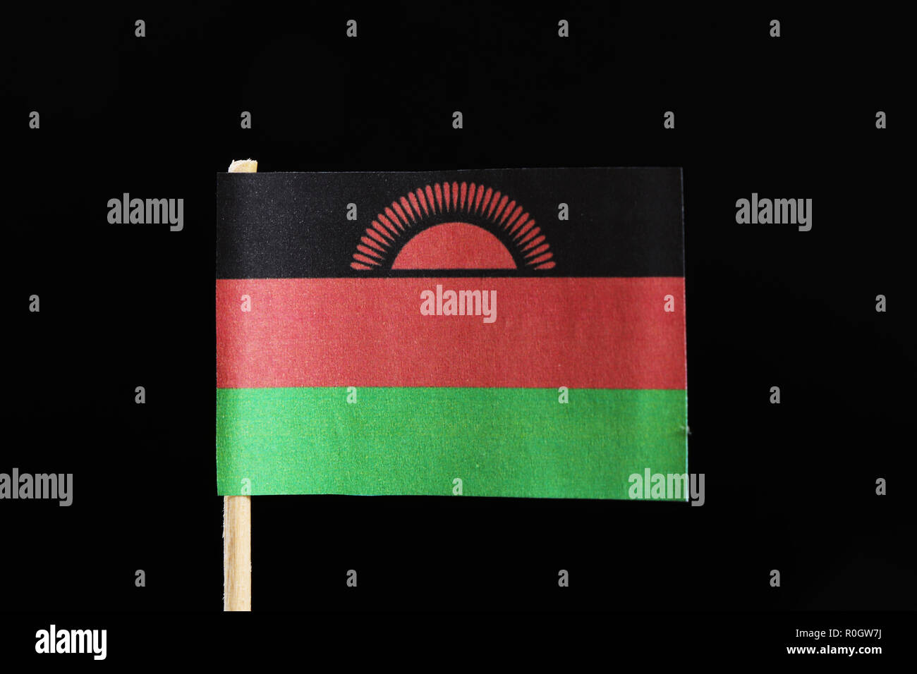 A original  flag of Malawi on toothpick on black background. Consists of a horizontal triband of black, red and green. Charged with a red rising sun w Stock Photo