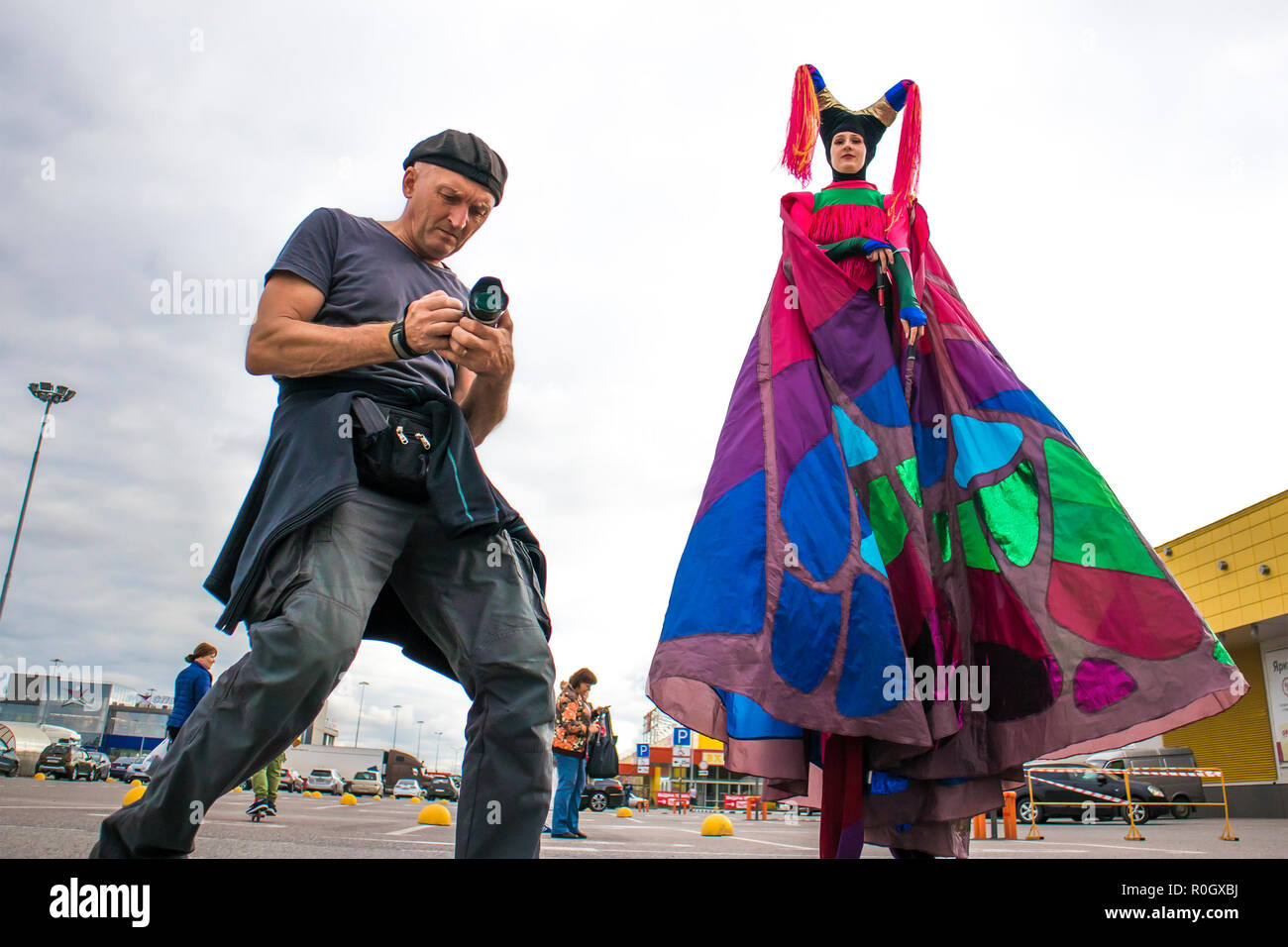 Young woman animator on stilts communicates with photographer on a large parking near big hypermarket Stock Photo