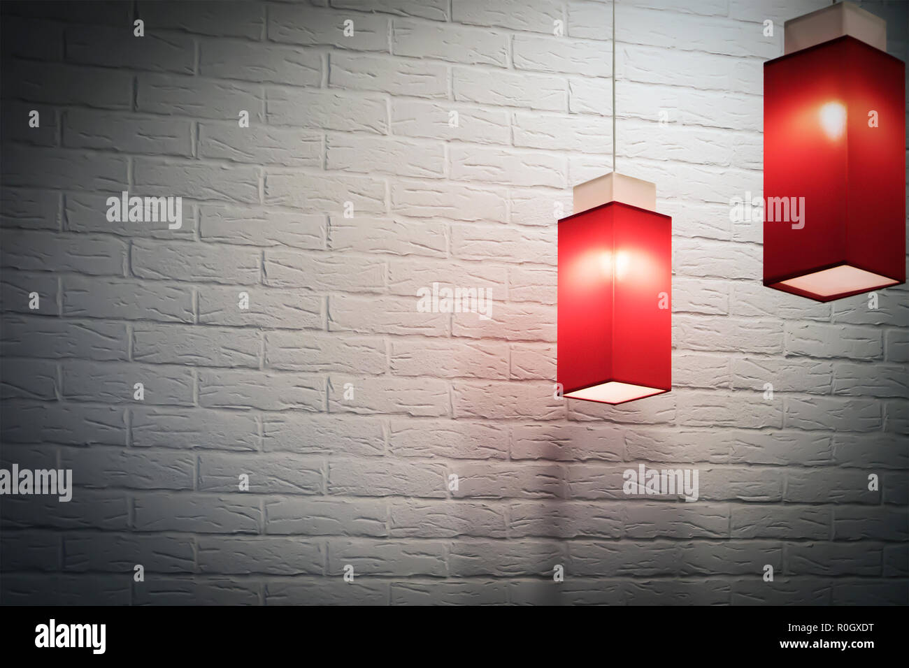 wo red elongated square pendant electric lamps against white brick wall, darkened vignette Stock Photo