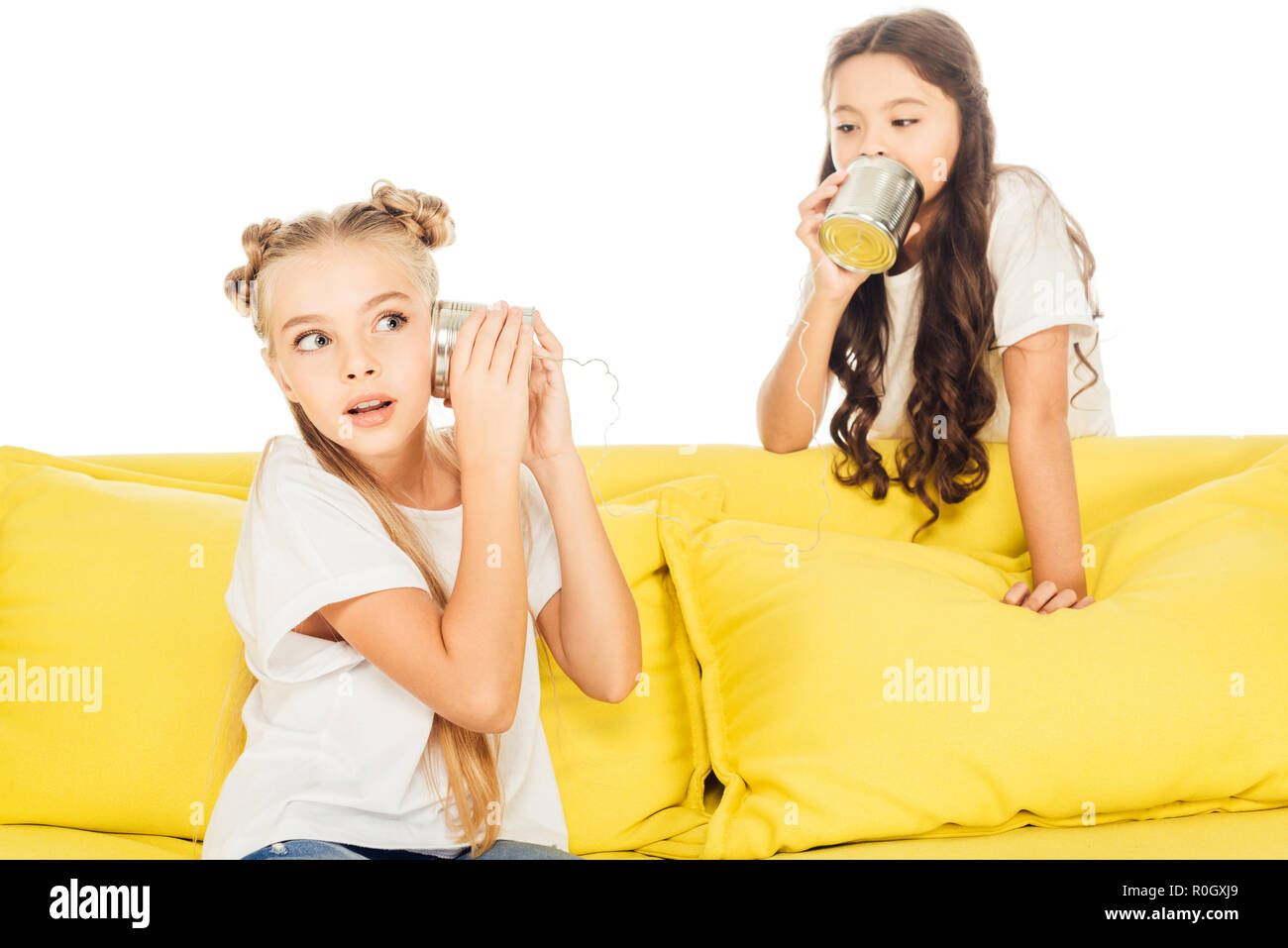 excited kids playing with tin cans phone on yellow sofa isolated on white Stock Photo