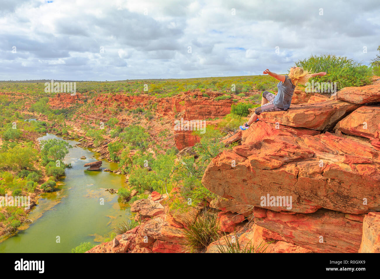Happy blonde woman with open arms on red sandstone rock at Hawks Head lookout over Murchison River in Kalbarri National Park, Western Australia.Freedom caucasian traveler enjoying outback of Australia Stock Photo