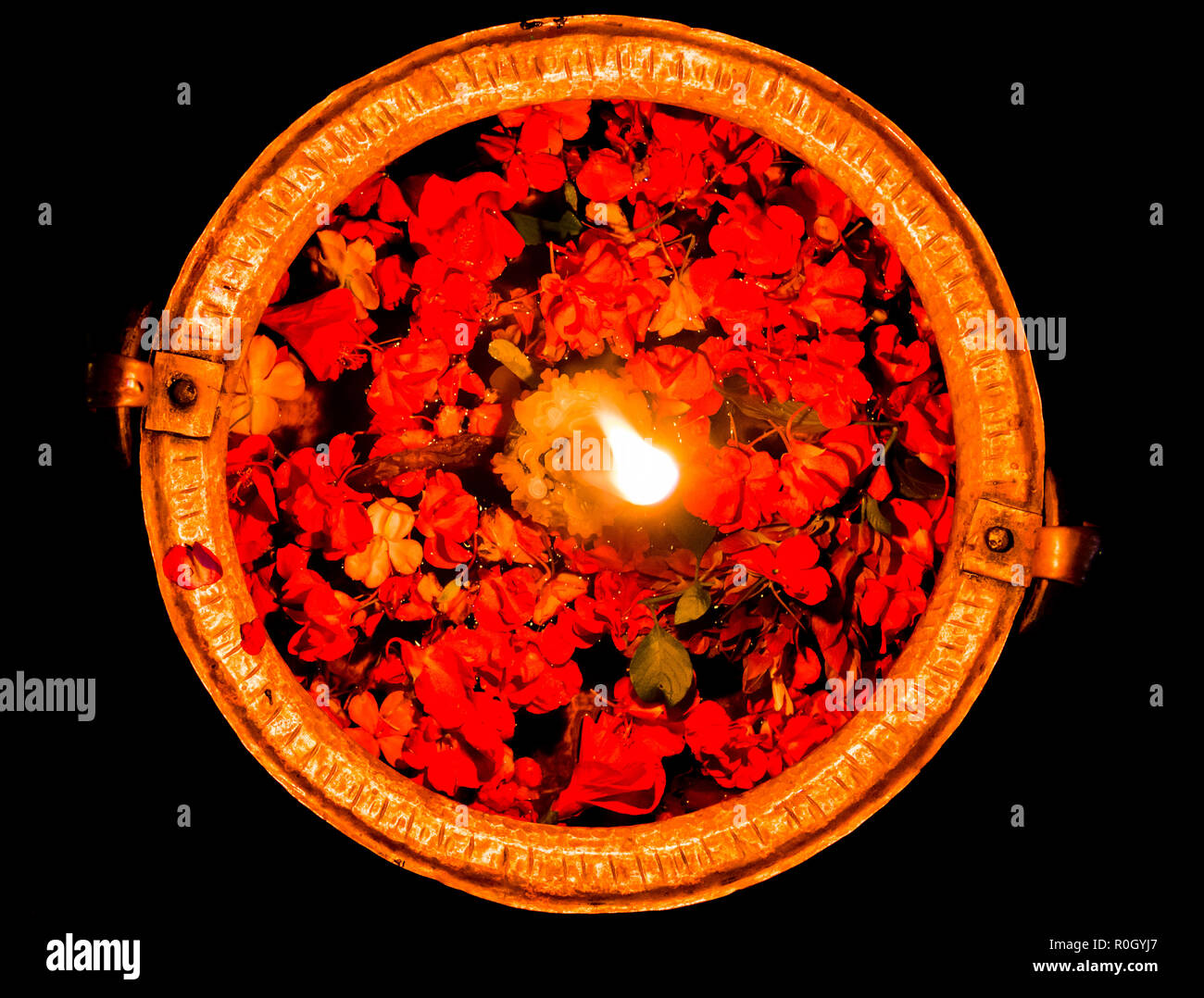 Water bowl with flower petals and lit candle in the middle, top view