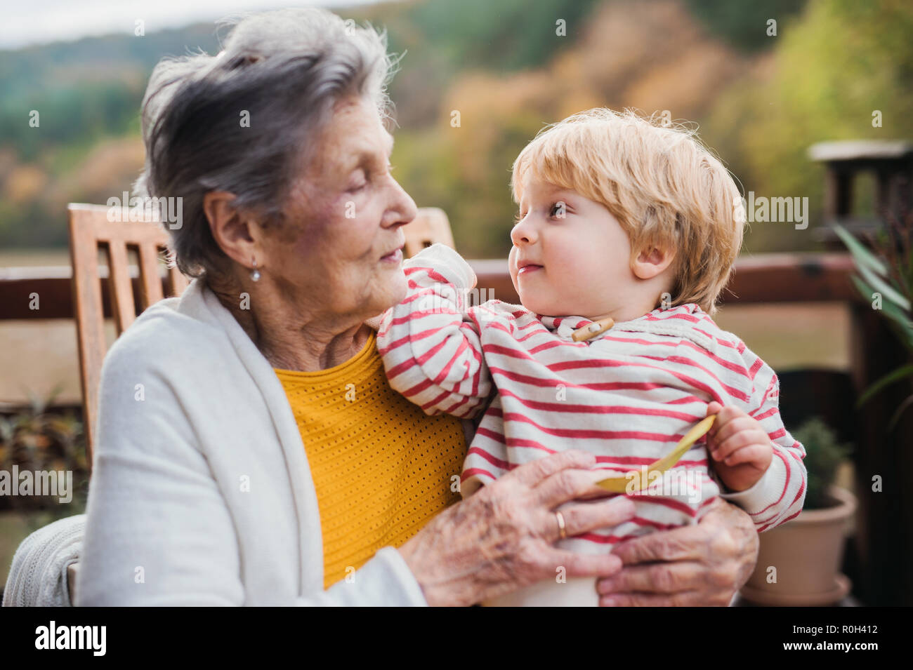 Elderly woman with a toddler great-grandchild on a terrace in autumn. Stock Photo