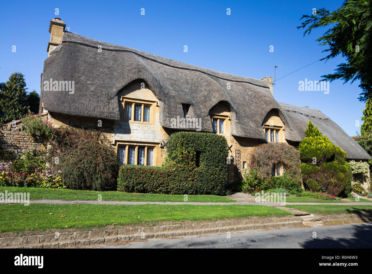 View of traditional Cotswold stone thatched cottage along Westington in autumn afternoon sunshine taken from public footpath Stock Photo