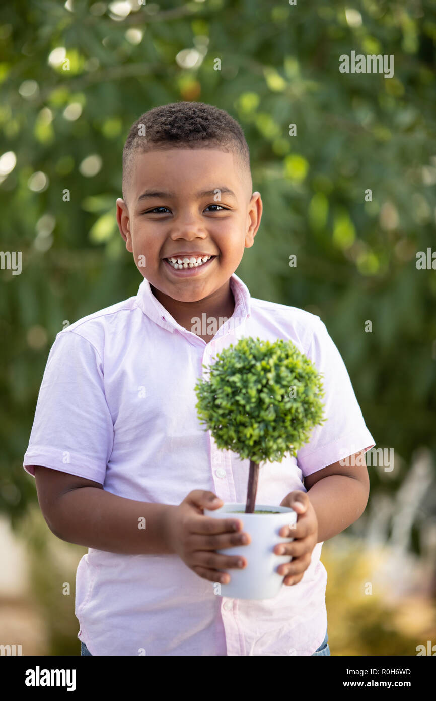 Happy latin child with a small tree in the garden Stock Photo