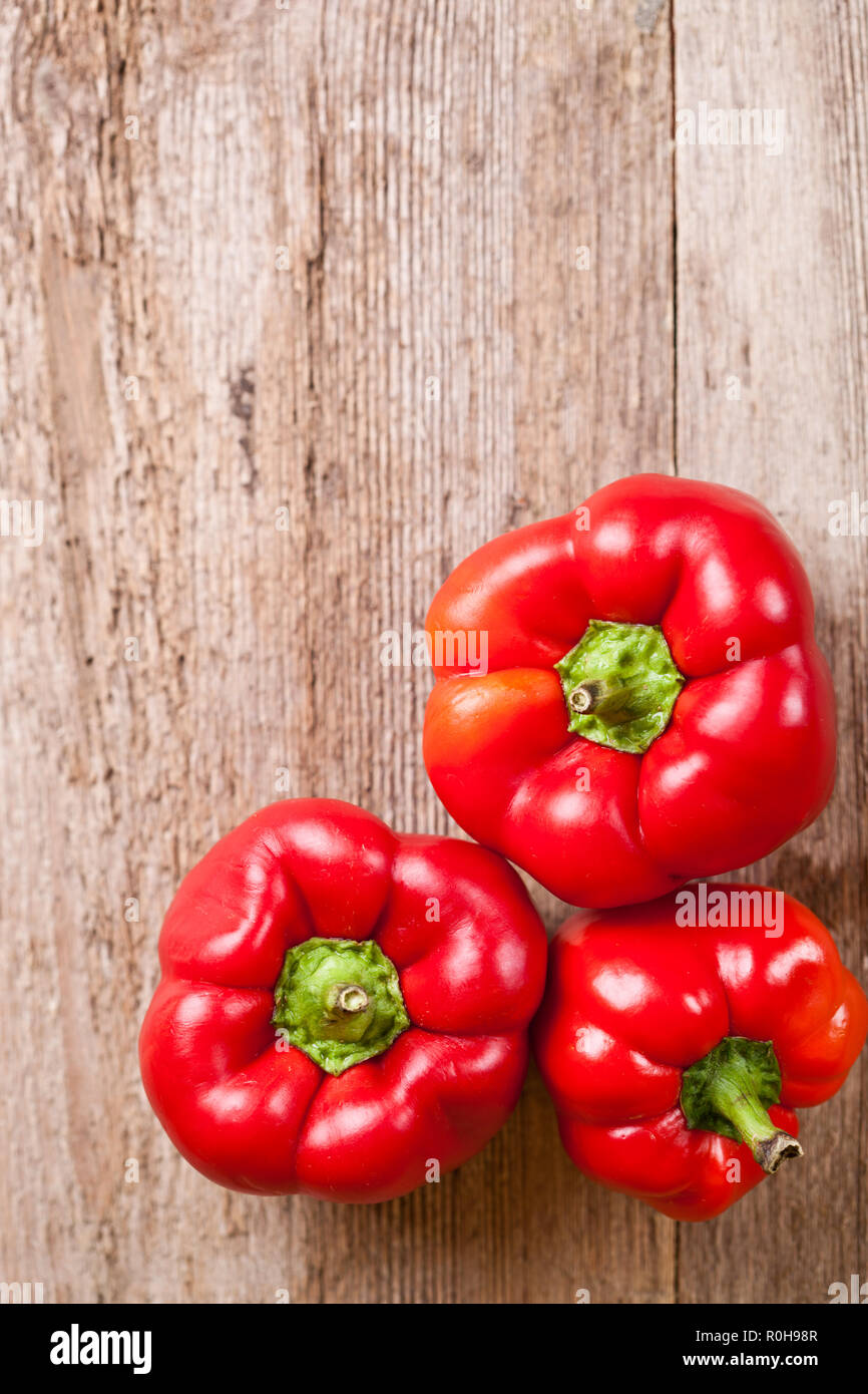 three red bell peppers on rustic wooden table Stock Photo - Alamy