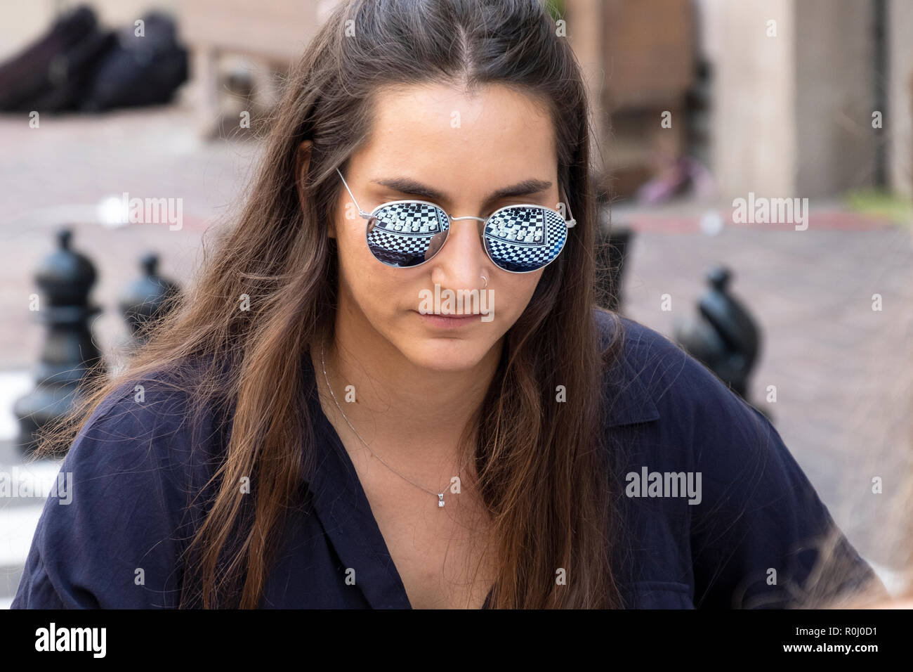 A young lady playing chess with reflection of the chess board in her sunglasses. in Tel Aviv, Israel in the Carmel Market. Stock Photo