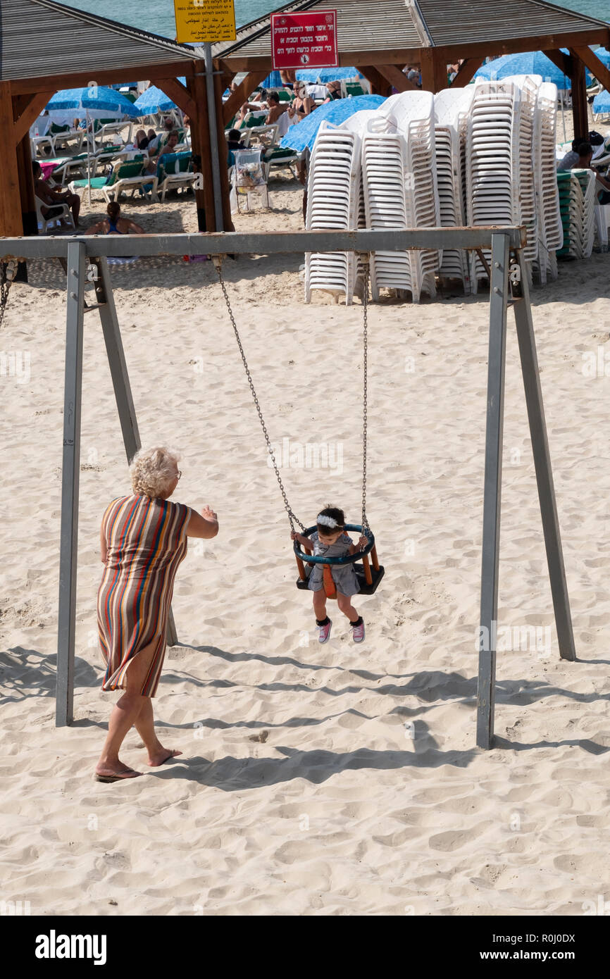 A grandmother pushing her grandchild on a swing on the beach in Tel Aviv, Israel. Stock Photo