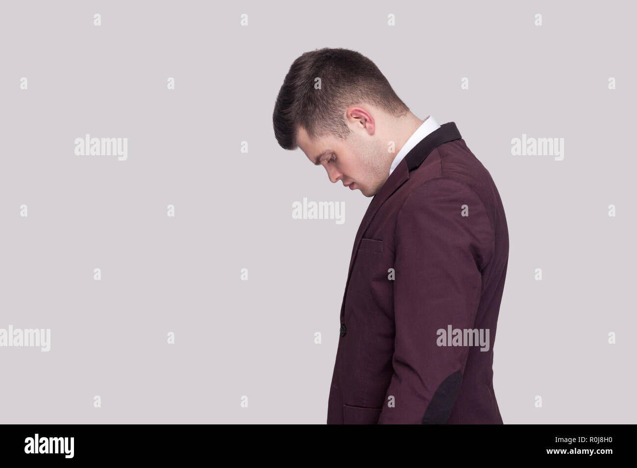 Profile side view portrait of sad handsome young man in violet suit and white shirt, standing and looking down with head down and bad mood. indoor stu Stock Photo