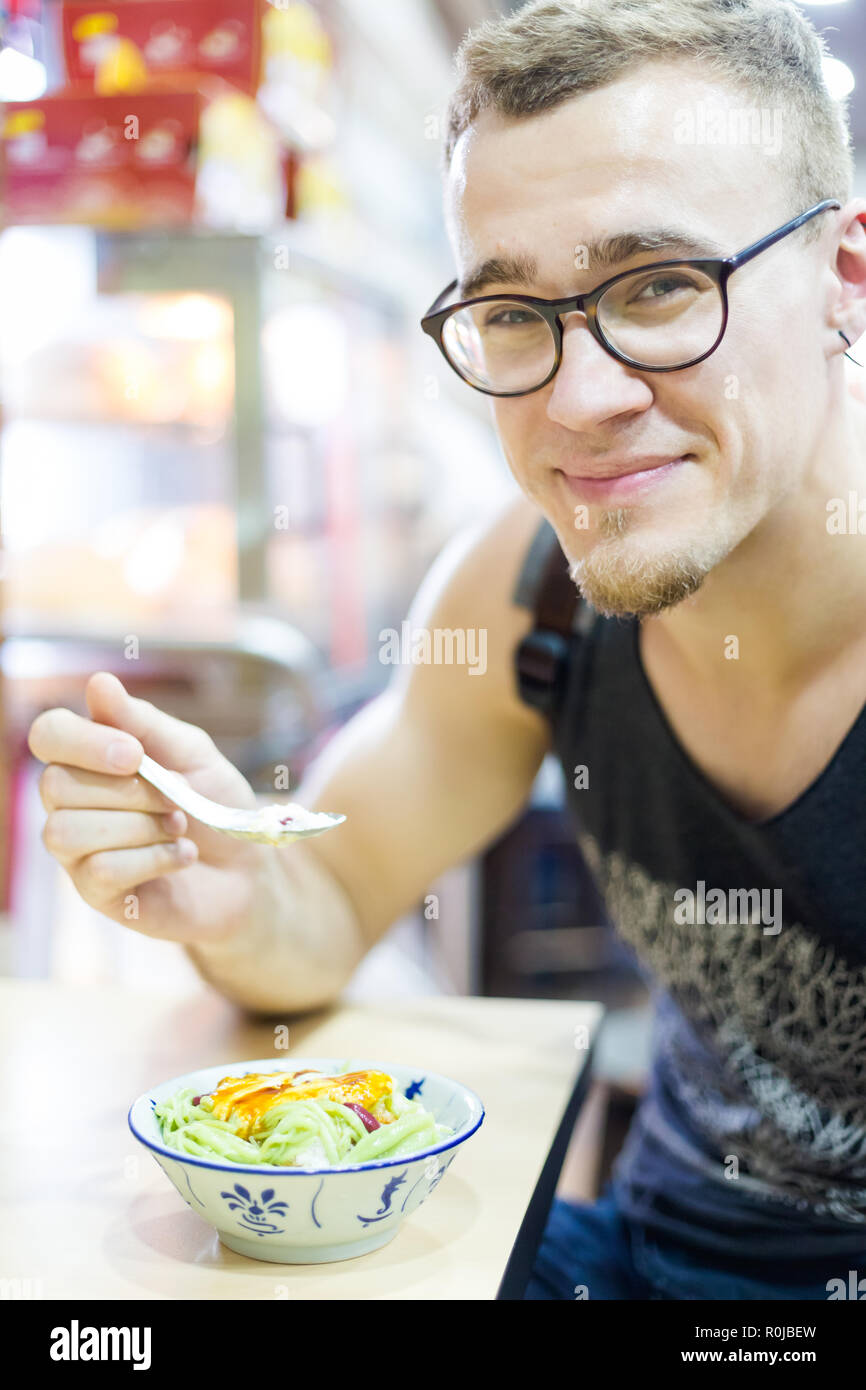 Young tourist eating cendol ais Kachang dessert in Mallaca city. Traditional shaved ice snack of Malaysia. Stock Photo