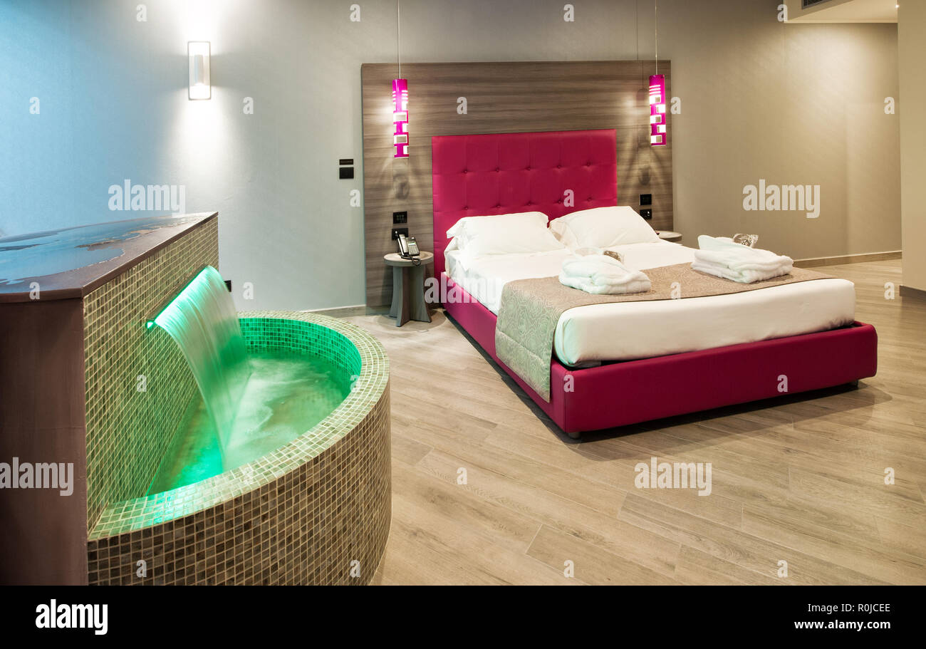 Modern motel bedroom in a luxury suite with green tiled water feature and a double bed with illuminated lamps and headboard Stock Photo