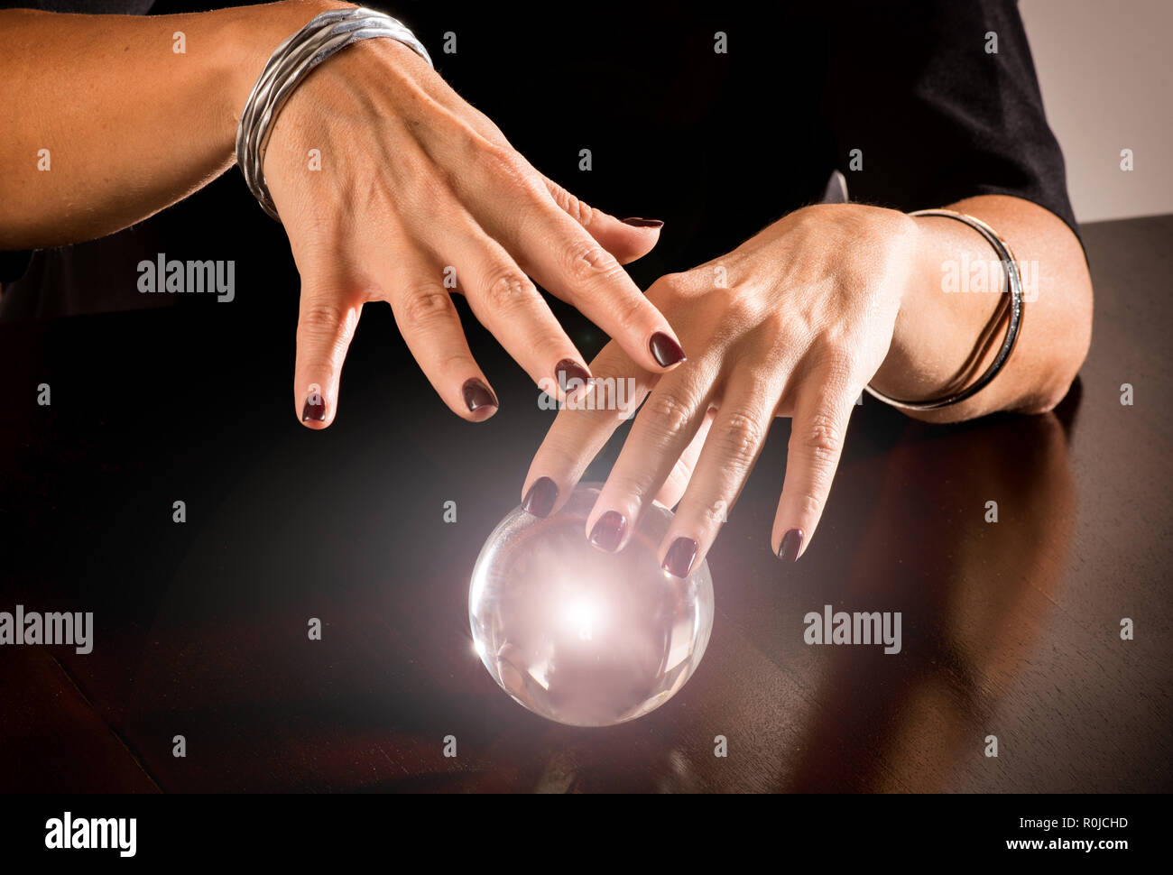 Fortune teller predicting the future on a magical glowing glass or crystal sphere in a close up view of her hands hovering over the orb Stock Photo