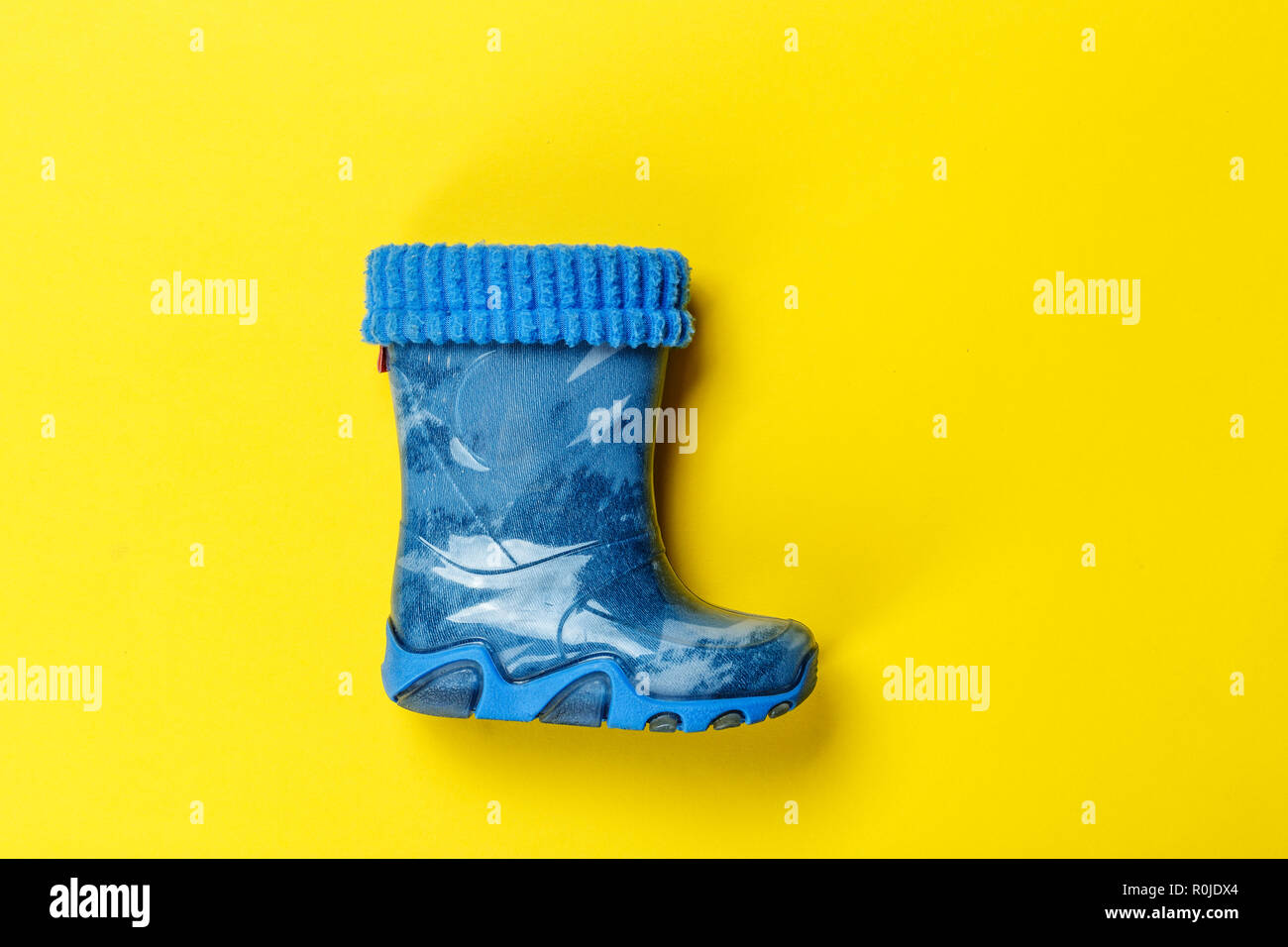one blue rubber boots on child boy on yellow background. autumn shoes ...