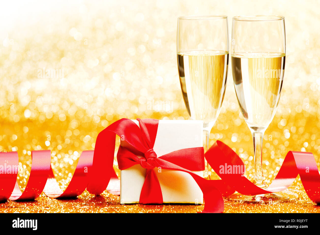 Champagne glasses and present in whitebox with red ribbon on golden background Stock Photo