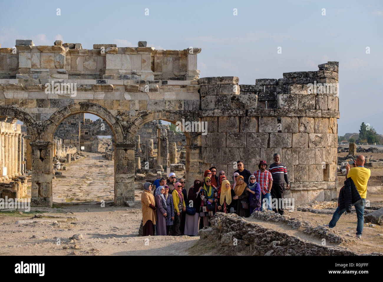 Muslim tour group taking photos in front of the ruins of the Frontinus Gate in the ancient Roman city of Hierapolis, Turkey Stock Photo