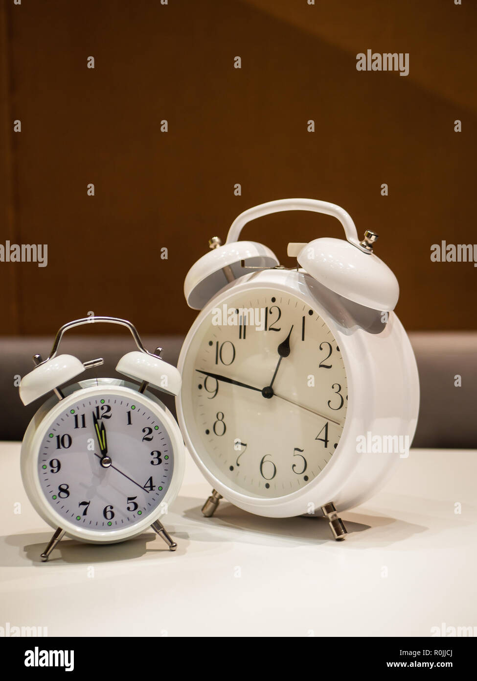 Two Vintage Alarm Clocks standing on a white desk with brown blurry sofa in background Stock Photo