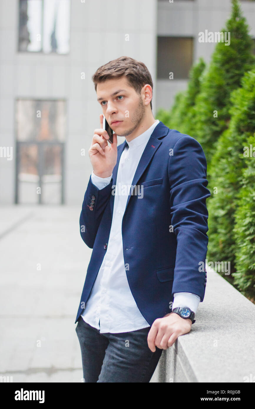 Business style. A young businessman is talking on the phone from the street. The guy in the blue jacket Stock Photo