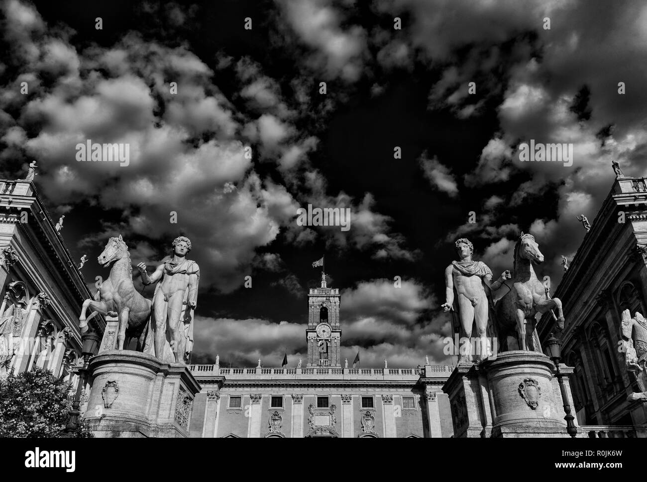 Capitoline Hill with ancient roman statues and renaissance clocktower with clouds, in the very center of Rome (Black and White) Stock Photo