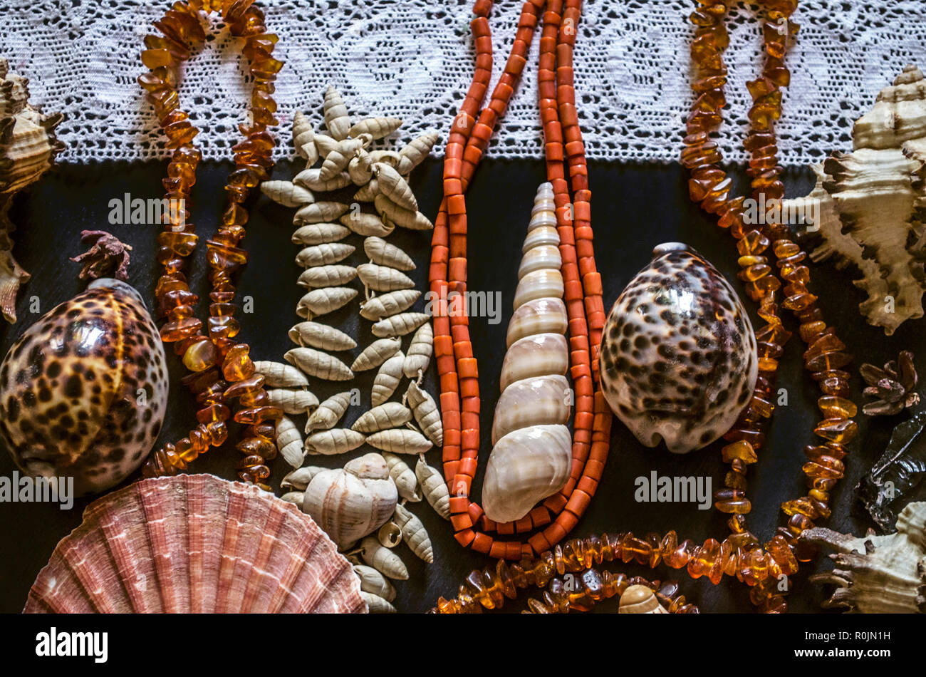 Various shells and stones with beads of red coral and small amber on the white openwork border lie on black plywood Stock Photo