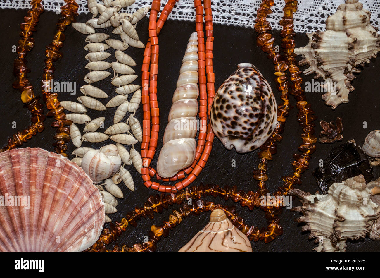 A group of shells and stones with amber and coral beads on a white openwork border lie on black plywood Stock Photo