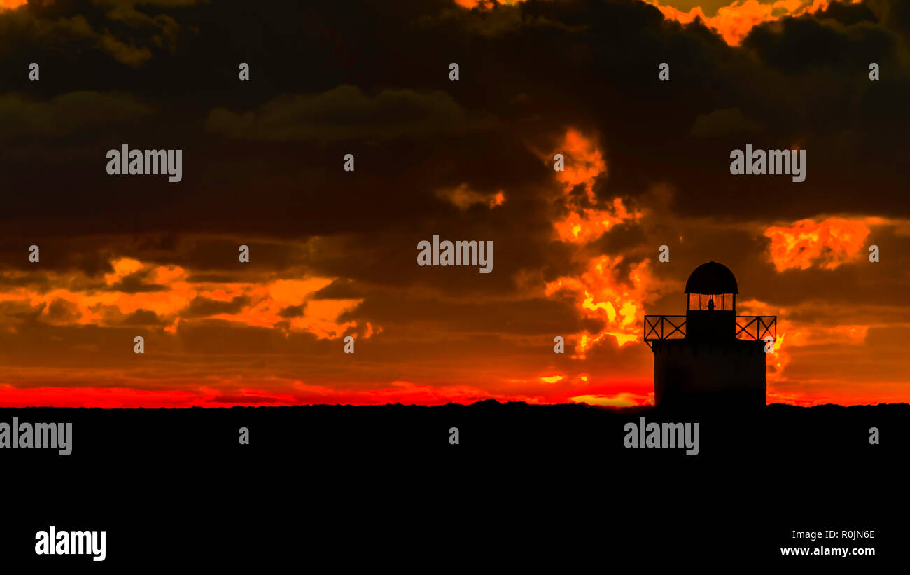 Silhouette of a lighthouse at sunset with clouds a red and orange background Stock Photo