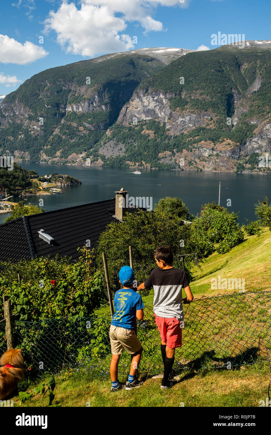 Two boys hanging on a fence looking at the view down to the town centre of Aurlandsvangen and the Sognefjorden fiord. Stock Photo