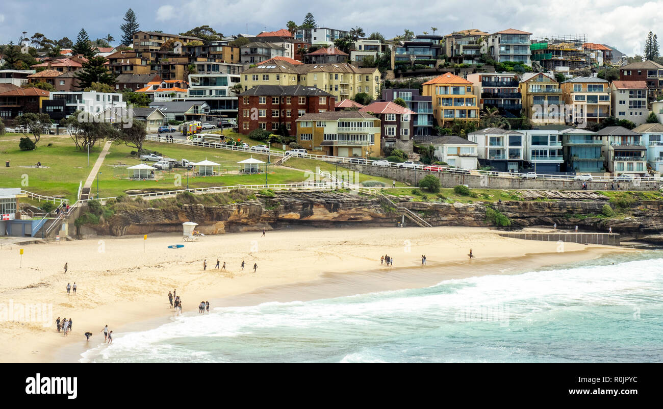 Bondi to Coogee coastal walk and people walking on the sand of Bronte Beach and dwellings on sandstone cliff over Pacific Ocean Sydney NSW Australia. Stock Photo
