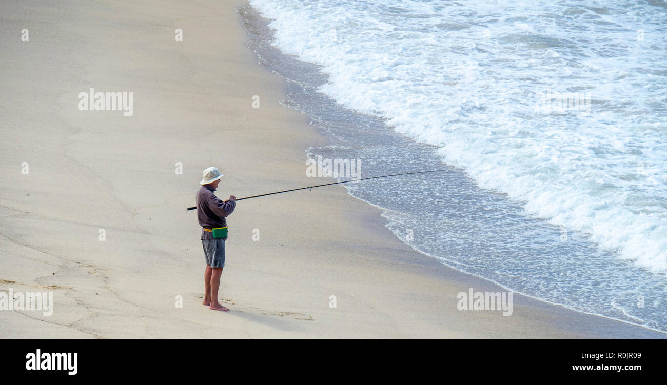 Lone male fisherman fishing with a fishing rod from the sandy Bronte Beach Sydney NSW Australia. Stock Photo