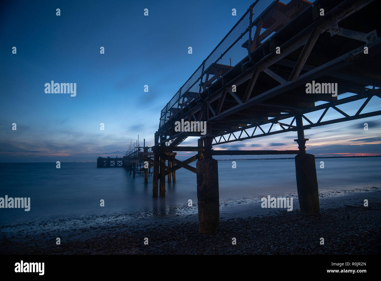 A broken and disused pier in Totland bay in the Isle of Wight with the night sky and a calm sea in the background Stock Photo