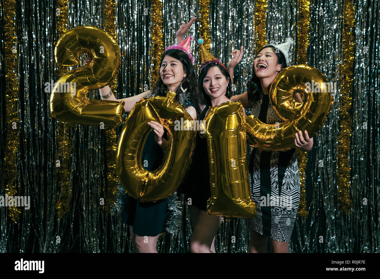 cheerful ladies showing gold number 2019 balloon at nightclub. new year eve party countdown with funny girls on the stage dancing with hats. young peo Stock Photo