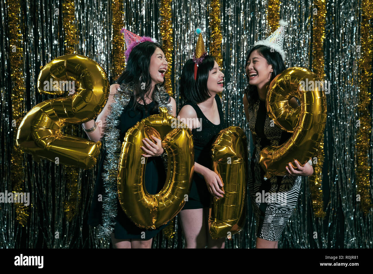 Celebrating New Year party group of cheerful young girls wearing dresses carrying gold colored numbers 2019 balloon. attractive beautiful ladies chatt Stock Photo