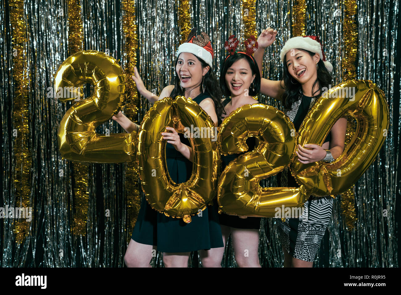 asian ladies having fun carrying gold 2020 balloon dancing in nightclub. cheerful young girls cill out celebrating new year eve with santa clothes. pa Stock Photo