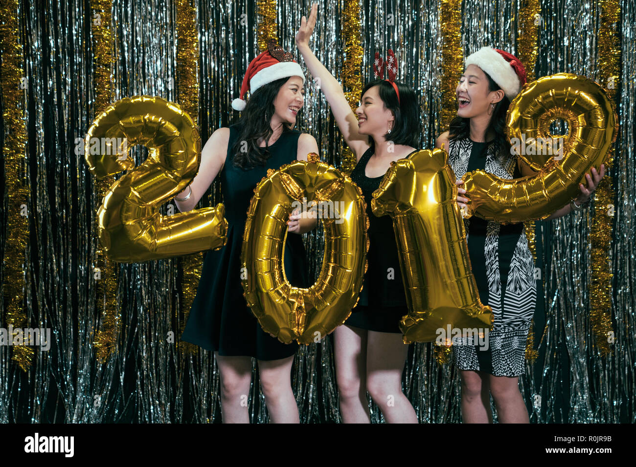 ladies with santa hats and deer costumes having fun dancing with gold 2019 new year balloon on party. happy beautiful attractive winsome glamorous gor Stock Photo