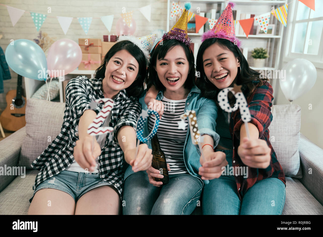 attractive girls celebrating new year eve house party. young friends showing 2019 number to the camera smiling cheerfully sitting on couch. beautiful  Stock Photo