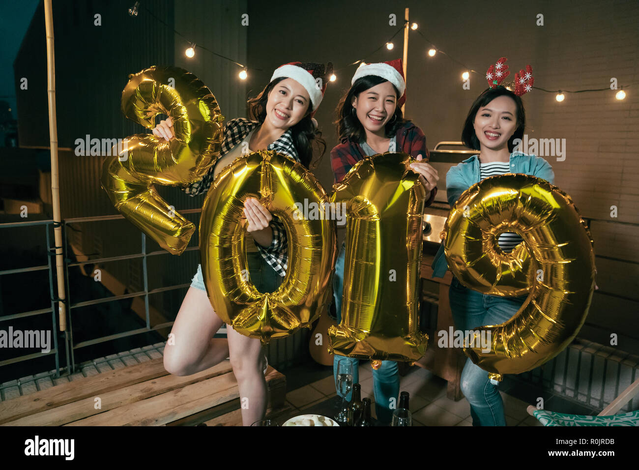 cheerful ladies enjoy music on balcony celebrating holding gold 2019 balloons on new year eve party. young girls with christmas costume outdoor at nig Stock Photo