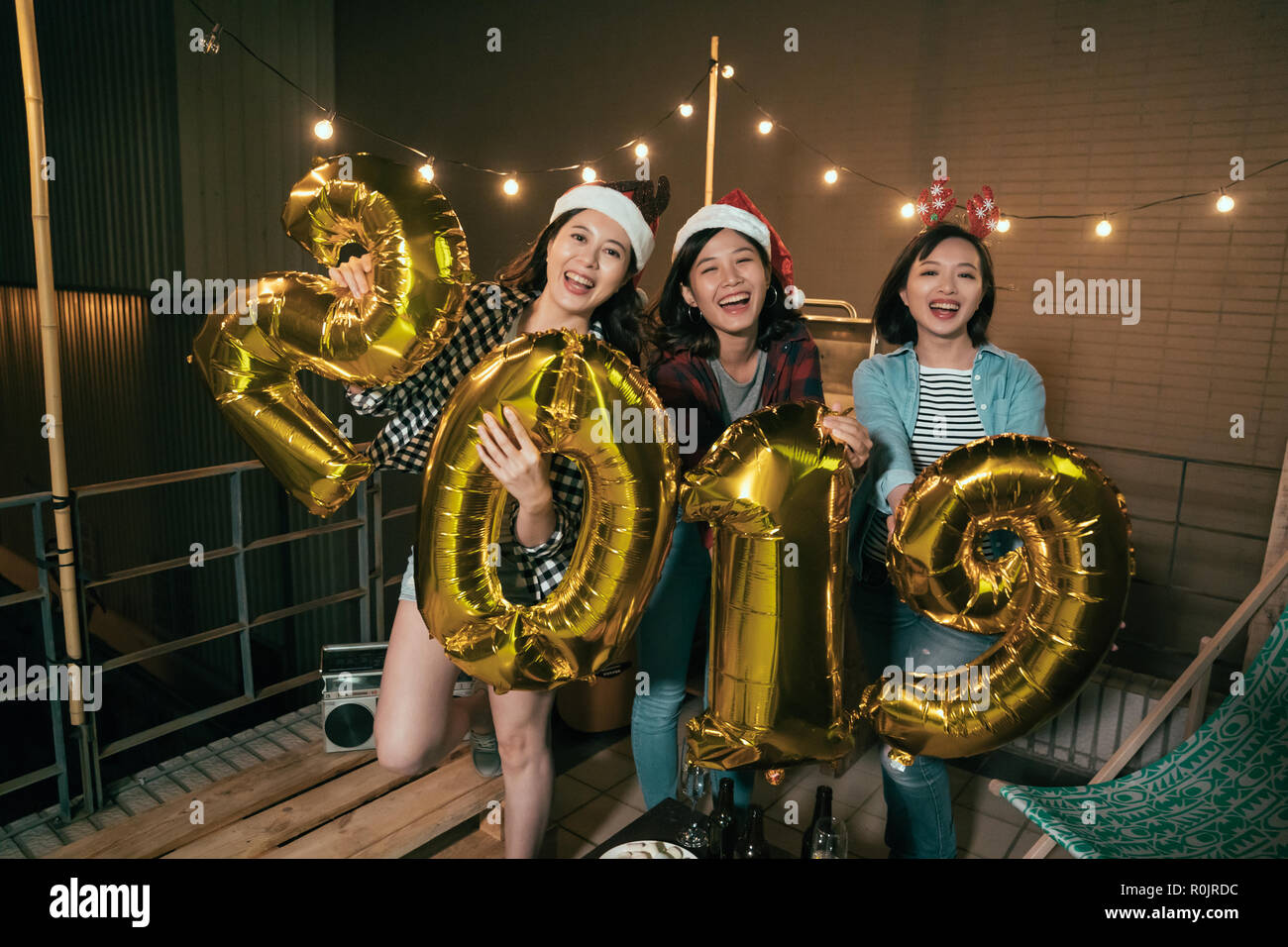 asian ladies enjoy music on balcony celebrating new year eve outdoor. young girls showing 2019 balloons on the roof at night. group of best friends en Stock Photo