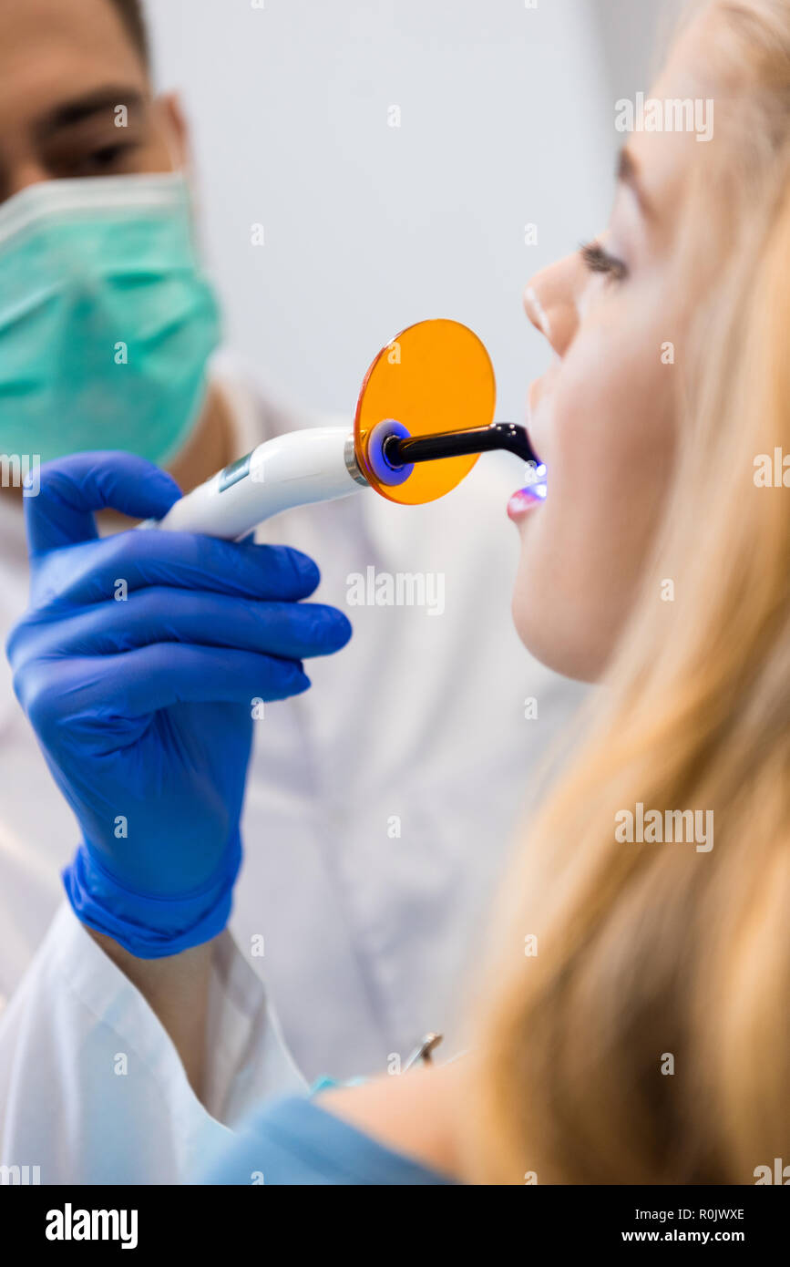 young dentist with dental curing light working with female client Stock