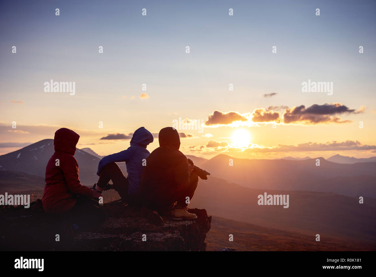 Three friends sits at the rock ang looks at mountains and sunset. Travel or active tourism lifestyle concept Stock Photo